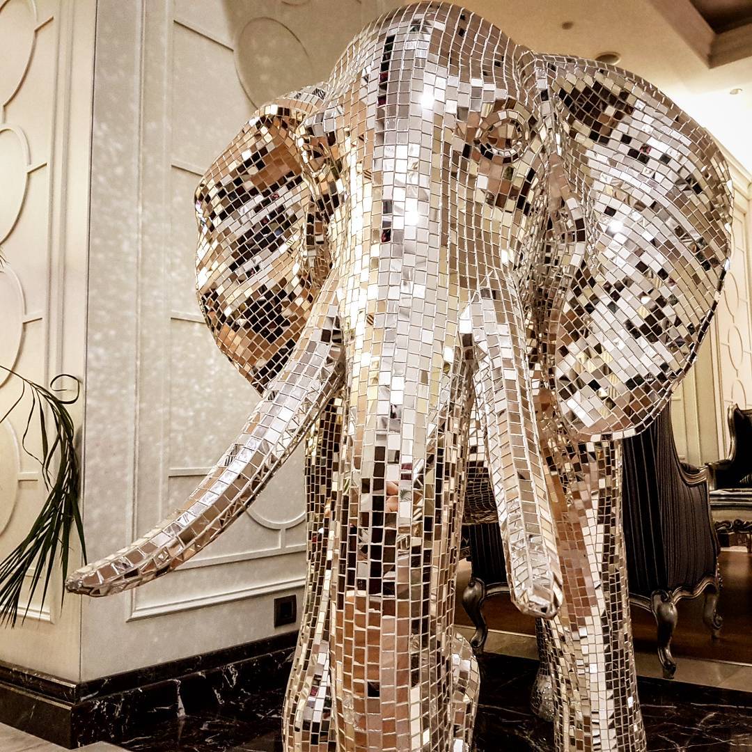 Life-size elephant sculpture covered entirely in mirror mosaic tiles standing in an ornate hotel lobby