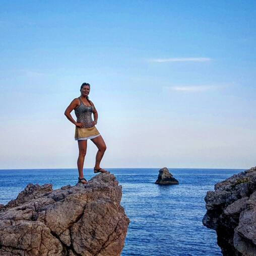 Woman standing hands on hips on a limestone outcrop above a deep blue sea, a single rock stack offshore behind her
