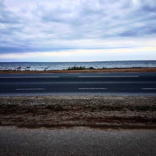 Empty coastal road with the flat grey sea beyond, heavy cloud filling the sky above the horizon