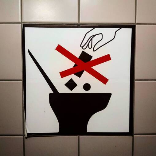 Black and white pictogram on white tiles showing a hand dropping objects into a toilet, struck through with a red cross