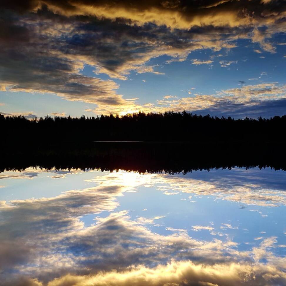 Sunset clouds mirrored so perfectly in a still lake that the treeline splits the frame into two identical skies