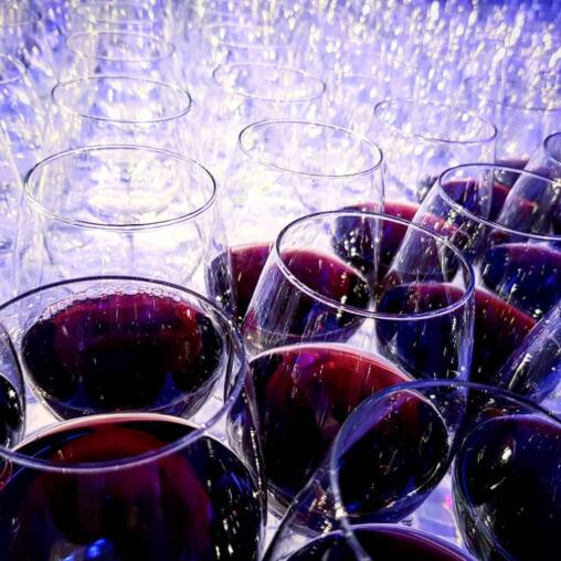 Rows of stemless wine glasses part-filled with red wine on a bar, lit from behind in violet blue