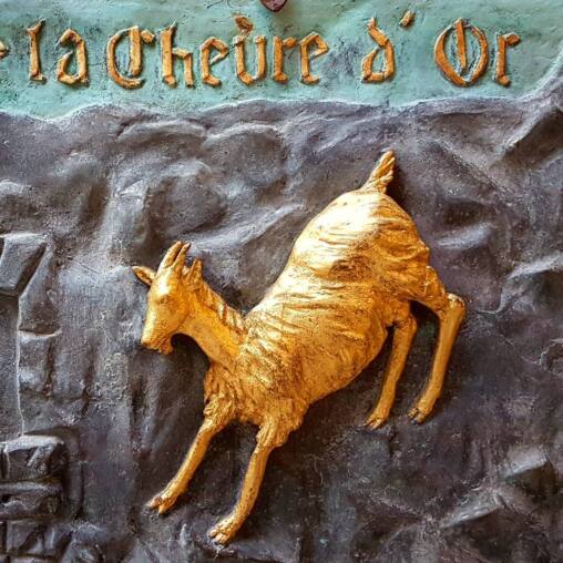 Bronze relief sign of a gilded goat leaping from rock, lettered La Chèvre d'Or above in gold