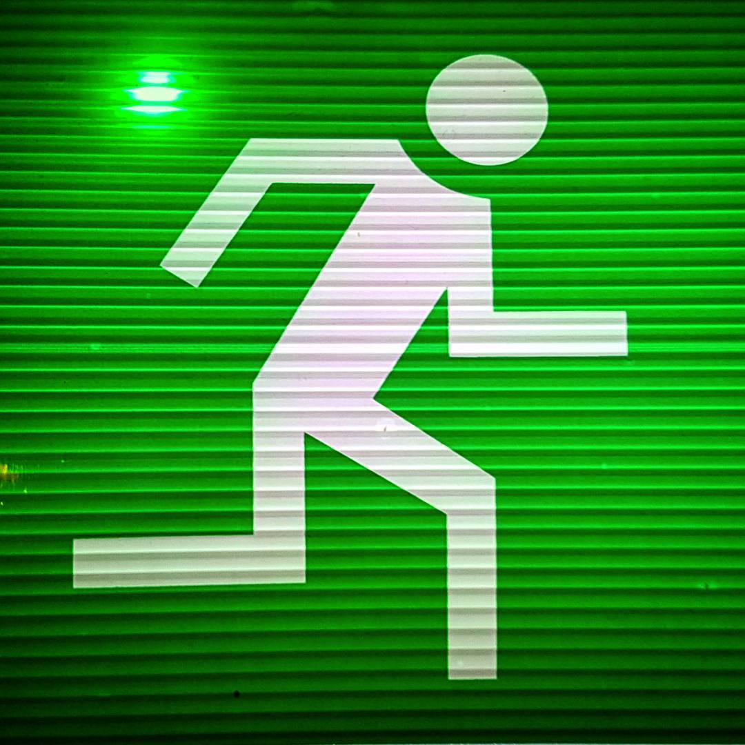 Illuminated green emergency exit sign, the white running figure filling the frame behind a ribbed diffuser