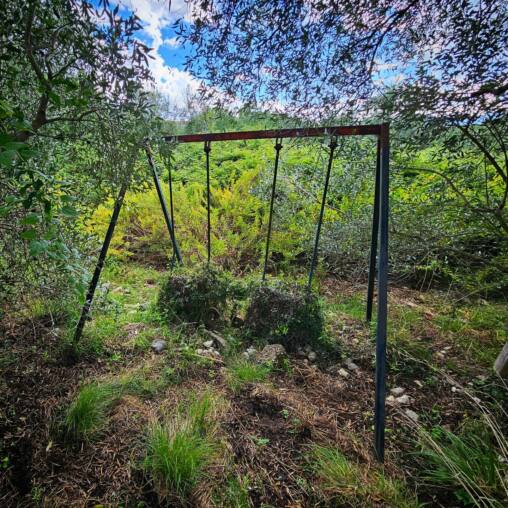 Rusty swing frame standing empty on an overgrown hillside
