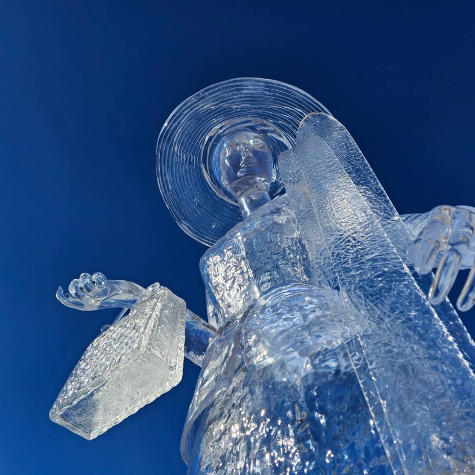 Transparent ice sculpture of an angel against a deep blue background