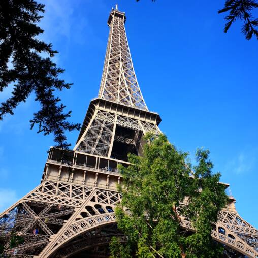 The Eiffel Tower seen from directly beneath its legs against a deep blue sky, with trees around the base