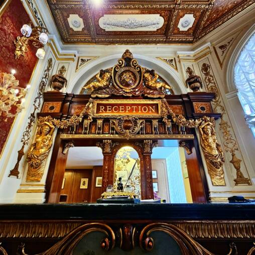 Gilded carved hotel reception desk with a red and gold interior behind it
